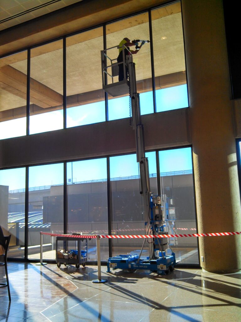 Installer on a lift applying window film in an airport terminal