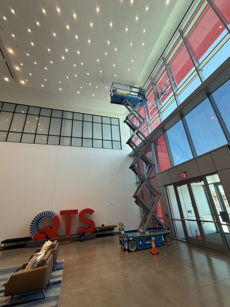Tall atrium glass wall being filmed from a scissor lift